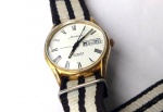 Vintage Coleção, Decoração, Relógio Retrô da Mondaine Swiss 25J Automático, Funcionando Dourado medindo 34mm de diâmetro. Branco com Algarismos Romanos, Segundeiro Central, Calendário Duplo, Fundo em Aço de Rosca, Pulseira Lonada Bicolor usada boa. 
