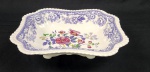 SPODE. Antiga fruteira/centro de mesa em porcelana inglesa branca, padrão
Mayflower, apresenta arranjo floral central detalhado com rosas e folhas
policromadas cercada por borda estilo `gadroon` com curvas e espirais envolta com
guirlanda florais azuis, medindo 6x28x23,5cm.