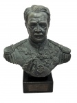 Antigo e imponente busto escultórico representando figura militar de alta patente, ricamente trajada com uniforme de gala ornamentado por medalhas, condecorações e dragonas em relevo. Escultura em composição patinada, apoiada sobre base retangular em pedra, apresentando assinatura/incisão na parte posterior. Medidas: 26,5 x 12,5 x 30,5 cm.