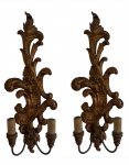 Antigo par de arandelas de parede em madeira ricamente entalhada, apresentando elegante decoração em motivos vegetalistas e volutas em estilo clássico. As peças possuem braços em metal para duas lâmpadas cada. Medidas: 59 x 35,5 x 15 cm.