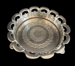 Delicada e antiga pequena bandeja em metal espessurado a prata, ricamente ornamentada com borda vazada em formato ondulado, decorada com detalhes florais em relevo. O centro apresenta fino trabalho gravado. Medidas: 11,5 x 4 cm.