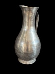 Antiga jarra em metal espessurado a prata, de elegante formato bojudo com gargalo alongado e delicado bico vertedor, ornamentado por discretos frisos em relevo. Possui alça lateral em desenho simples e funcional, além de base canelada. Medidas: 27 x 14 x 15 cm.