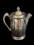 Antiga chocolateira em metal espessurado a prata, de elegante formato bojudo com corpo em suaves gomos verticais. A peça apresenta rica ornamentação em relevo no bico vertedor e na alça, ambos com desenho elaborado de inspiração clássica. Tampa abaulada com delicado arremate superior decorativo. Medidas: 25 x 27 x 14 cm.