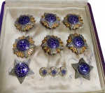 Conjunto de insígnias e condecorações militares brasileiras em metal esmaltado, acondicionadas em estojo original forrado. O lote é composto por peças com estrela de cinco pontas e esmaltação nas cores azul, branca, amarela e vermelha, incluindo miniaturas e distintivos de lapela. Peças de interesse histórico e colecionável, relacionadas a ordens honoríficas e memorabilia militar brasileira. Med: 4 cm