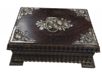 Antiga caixa de madeira nobre, de formato retangular, ricamente ornamentada com aplicações e guarnições em prata, apresentando motivos florais em relevo na tampa e cantoneiras decorativas, apoiada sobre quatro pés, com acabamento entalhado nas bordas. Med.: 19,5 x 14 x 7 cm.