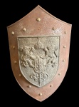 Escudo decorativo em metal, em formato heráldico, apresentando brasão em relevo ao centro com coroa e leões rampantes, aplicado sobre base patinada com rebites aparentes. Peça de caráter ornamental, inspirada em modelos medievais/europeus, ideal para composição decorativa de ambientes rústicos ou temáticos. Medidas; 60,5 x 41 x 10 cm. Apresenta oxidação.