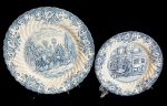 Dois pratos decorativos em faiança inglesa Johnson Bros, padrão Coaching Scenes, com cenas campestres e diligências em tonalidade azul sobre fundo branco. Bordas ricamente ornamentadas com motivos florais e volutas em relevo, apresentando acabamento recortado. medindo: 19,5 cm e 25 cm.