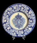 Medalhão em cerâmica artística brasileira, assinado Luiz Salvador  Itaipava, ricamente ornamentado em tons de azul sobre fundo branco. Ao centro, destaca-se brasão heráldico de inspiração portuguesa, cercado por exuberantes arabescos em relevo executados manualmente. Brasil, séc. XX. Med.: 36 cm de diâmetro.