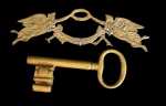 Duas peças em bronze, sendo uma antiga chave decorativa de grandes dimensões e um porta-chaves de parede ornamentado com figuras de aves e detalhes em relevo. Medidas: chave 20,5 x 10 x 3 cm; porta-chaves 30 x 8 x 2,5 cm.