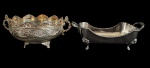 Duas peças em metal espessurado a prata, sendo uma fruteira/cachepot de formato circular ricamente ornamentada em relevo e apoiada sobre pés, e uma pequena floreira ou centro de mesa retangular com alças laterais e pés decorativos, ambas apresentando pequenos desgastes no banho compatíveis com o tempo. Medidas: 18 x 13,5 x 7,5 cm e 19 x 10,5 x 6 cm.