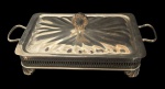 Suporte em metal espessurado a prata, de formato retangular com tampa e alças laterais, apoiado sobre pés ornamentados, NÃO acompanhando o refratário em pirex, medindo ; 35x17x13cm.
