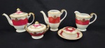 Meito, Japan. Conjunto para servir em porcelana japonesa esmaltada, pintada à mão, com interior em tom vinho e rica decoração em arabescos com detalhes em ouro. Composto por bule de chá, bule de café, leiteira, manteigueira e açucareiro. Manufatura no verso. Observação: Bule de café e chá com bico colado.