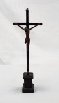 Crucifixo em madeira com Cristo esculpido, fixado sobre cruz e base também em madeira, medindo 44 cm de altura total, apresentando desgaste natural do tempo, fissuras e marcas de uso.