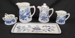 Steatita, Brasil. Cinco peças para servir em porcelana esmaltada, com decoração floral azul estilo cebolinha. Composto de jarra, bule, leiteira, açucareiro, travessa para rocambole e 2 colheres. Manufatura no verso. Medindo: 39 cm bandeja. Leiteira com lasca, bule com pequeno restauro.