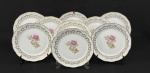 Porcelana Schmidt. Nove belíssimos pratos rasos em porcelana esmaltada, decorados com motivos florais e ricos detalhes em ouro. Bordas onduladas, ramos nas extremidades em relevo e filetes em ouro Manufatura no verso. Medindo: 24,5 cm. Um com bicado.