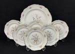 C. Tielsch & Co., Polônia, década de 1940. Conjunto para sobremesa em porcelana esmaltada na cor branca, decorados com delicados ramalhetes florais em policromia, frisos dourados e bordas onduladas. Composto de prato para bolo e 6 pratos para sobremesa. Manufatura no verso. Medindo:32 cm e 19 cm.