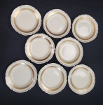 Vista Alegre, Portugal. Oito pratos para pão em porcelana portuguesa esmaltada na cor creme, com frisos em ouro. Manufatura no verso. Medindo:15 cm.