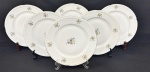 Seis pratos rasos em porcelana da República Tcheca, esmaltados na cor branca, decoração floral policroma e filetes em ouro, bordas com ramos em relevo. Med. 24,5 cm diâm.