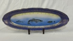 Porcelana Real. Travessa oval em porcelana nacional esmaltada, decoração com peixes em policromia sobre fundo branco e azul, ricamente realçada a ouro. Bordas ornamentadas em azul cobalto com delicados motivos em ouro. Manufatura no verso. Medindo 23 x 63 cm.