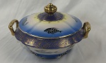 Porcelana Real. Terrina em porcelana nacional esmaltada, decoração com peixes em policromia sobre fundo branco e azul, ricamente realçada a ouro. Bordas ornamentadas em azul cobalto com delicados motivos em ouro. Alças e pega da tampa com acabamento em ouro. Manufatura no verso. Medindo 18 x 27 x 23 cm.
