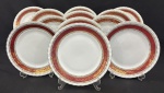 Steatita. Doze pratos rasos em porcelana nacional esmaltada, decoração com larga faixa na tonalidade vinho, enriquecida por minuciosos ornamentos geométricos e arabescos, ricamente realçados a ouro, sobre fundo branco. Manufatura no verso. Medindo: 24,5 cm. 4 com bicados.