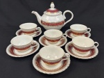 Steatita. Conjunto para chá em porcelana nacional esmaltada, decoração com larga faixa na tonalidade vinho, enriquecida por minuciosos ornamentos geométricos e arabescos, ricamente realçados a ouro, sobre fundo branco. Composto de 1 bule e 6 xícaras com os respectivos pires. Alt do bule: 18 cm.