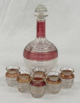 Garrafa licoreira estilo francês, anos 1950–60 (Mid-Century/Art Déco de transição), com tampa escalonada e seis copos. Em vidro transparente, com decoração em esmalte overlay nas cores rubi e translúcido, com filetes dourados, tampa em formato zigurate.
