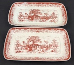 Schmidt. Duas travessas em porcelana esmaltada sobre fundo branco, decoração monocromática no tom grená representando cenas bucólicas de paisagem, com arquitetura rural, árvores e elementos campestres, circundadas por rica composição ornamental nas bordas. Manufatura no verso. Medindo: 32 x 18 cm e 35 x 20 cm. 