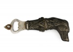 Abridor de garrafas executado em metal prateado, corpo vertical com empunhadura configurada em forma de cabeça de cão, com orelhas longas caídas, focinho alongado e tratamento superficial com texturização simulando pelagem. Transição para haste com elemento ornamental de motivo vegetalista, com volutas e folhagens em relevo; lâmina recortada destinada à remoção de tampas metálicas, integrada ao corpo por fundição. Apresenta marcas de uso. Medidas: Alt.: 17,5 x Comp.: 7 cm.