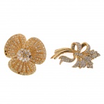 Par de broches em metal dourado, cravejados com pedras translúcidas facetadas. Um em composição floral trilobada, com engaste pavê e reservas raiadas; outro em composição fitomórfica com laçarote, folhagens e ramagens estilizadas, ambos com fechos metálicos de alfinete no verso. Medidas: Diam.: 4,5 cm; Comp.: 4,5 cm.