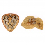 Par de broches em metal dourado, sendo um em formato escudiforme com volutas afrontadas cravejadas por pedras translúcidas facetadas, e outro em composição fitomórfica com folhas nervuradas e bolotas estilizadas ornadas por pedras translúcidas facetadas. Reversos com fechos metálicos de alfinete, um deles marcado Craft. Estado conforme fotografias. Medidas: Alt.: 5,5 x Comp.: 5 cm; Comp.: 6,5 x Larg.: 4 cm.