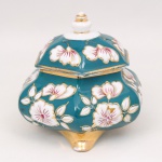 Bombonière em porcelana nacional de formato facetado, corpo bojudo apoiado sobre pés integrados, tampa abaulada com pega torneada. Decoração esmaltada em fundo azul-turquesa com reservas florais em branco e detalhes em rosa, contornados por douração. Bordas e pés realçados em ouro. Marca na base São José - Pedreira. Contém desgaste na douração, trincado na tampa e no fundo da base. Medidas: Alt.: 15,5 x Comp.: 17 x Larg.: 15 cm.