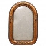 Moldura porta-retrato de formato retangular com arco pleno, executada em madeira entalhada e dourada, apresentando decoração em relevo composta por volutas, folhagens e florões estilizados distribuídos simetricamente na parte superior, inferior e laterais. A moldura é delimitada por frisos paralelos e possui acabamento em douração. Verso em madeira com estrutura montada por encaixes. Medidas: Epelho: Alt.: 49,5 x Comp.: 29 cm. .Moldura: Alt.: 62 x Comp.: 41,5 cm.