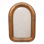 Moldura porta-retrato de formato retangular com arco pleno, executada em madeira entalhada e dourada, apresentando decoração em relevo composta por volutas, folhagens e florões estilizados distribuídos simetricamente na parte superior, inferior e laterais. A moldura é delimitada por frisos paralelos e possui acabamento em douração. Verso em madeira com estrutura montada por encaixes. Medidas: Epelho: Alt.: 49,5 x Comp.: 29 cm. .Moldura: Alt.: 62 x Comp.: 41,5 cm.