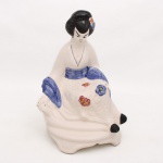 Escultura orientalista representando figura feminina trajando quimono, executada em faiança moldada e esmaltada, com decoração floral policromada em relevo e cabelos estilizados em esmalte preto. Base integrada de contorno recortado. Medidas: Alt.: 30 x Comp.: 20 x Larg.: 17 cm.
