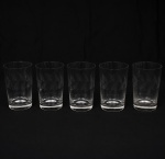 CRISTAL HERING. Elegante conjunto de tcopos em cristal, diáfano e incolor; bojo cilíndrico talhado com folhagens estilizadas dispostas em faixas horizontal, base circular espessada. Composto de cinco(05) unidades. Medidas: Alt.: 11 x Diam.: 7 cm.