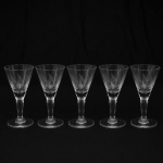 CRISTAL HERING. Elegante conjunto de taças para licor em cristal, diáfano e incolor; bojo obcônico talhado com folhagens estilizadas dispostas em faixas horizontal, fuste tubular, de topo facetado, sobre base circular. Composto de seis(05) unidades. Medidas: Alt.: 10,5 x Diam.: 5,5 cm.