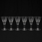 CRISTAL HERING. Elegante conjunto de taças para vinho do Porto em cristal, diáfano e incolor; bojo obcônico talhado com folhagens estilizadas dispostas em faixas horizontal, fuste tubular, de topo facetado, sobre base circular. Composto de seis(06) unidades. Medidas: Alt.: 12,5 x Diam.: 6 cm.