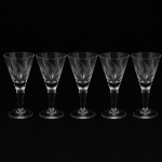CRISTAL HERING. Elegante conjunto de taças para vinho do Porto em cristal, diáfano e incolor; bojo obcônico talhado com folhagens estilizadas dispostas em faixas horizontal, fuste tubular, de topo facetado, sobre base circular. Composto de cinco(05) unidades. Medidas: Alt.: 12,5 x Diam.: 6 cm.