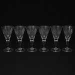 CRISTAL HERING. Elegante conjunto de taças para água em cristal, diáfano e incolor; bojo obcônico talhado com folhagens estilizadas dispostas em faixas horizontal, fuste tubular, de topo facetado, sobre base circular. Composto de seis(06) unidades. Medidas: Alt.: 17,5 x Diam.: 9 cm.