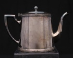 WOLFF. Elegante bule para café confeccionados em metal espessurado à prata, bojo aproximadamente cônico, bordas contornadas por barrados relevados com frisos intercalados por flores, padrão conhecido pelo senso comum como "florzinha"; tampa dotada de abertura através de movimento basculante, puxador circular, bico curvilíneo de ponta recortada, alça lateral curvada com descanso de polegar retilíneo. Marca da manufatura puncionada ao fundo. Meds.: Alt. 14,5 x Comp. 22,5  x Larg. 11,5 cm.