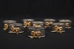 Conjunto composto por sete(07) argolas para guardanapo em metal prateado, de formato oblongo, decoradas na parte frontal com aplicação de laço em metal dourado. Alt.: 2,5 x Comp.: 5 x Larg.: 3,5 cm.