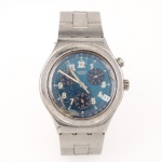 Relógio de pulso marca Swatch, modelo da linha Irony Chronograph, com caixa e pulseira em aço inoxidável. Mostrador em tonalidade azul com numeração arábica luminosa, três registros auxiliares para cronógrafo, calendário na posição de quatro horas e escala taquimétrica periférica. Fundo identificado Swatch Irony, Stainless Steel, Water-Resistant e Four (4) Jewels. Movimento a quartzo de fabricação suíça. Apresenta pulseira articulada metálica com fecho dobrável gravado Swatch. Década de 1990/2000. Não está funcionando, estado conforme fotografias, apresenta sinais de uso e desgastes.Medidas: Diam.: 40 mm.