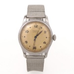 Relógio de pulso Pronto Automatic, executado em aço, caixa circular com mostrador patinado em tonalidade creme, apresentando algarismos arábicos aplicados, escala perimetral de minutos e ponteiros centrais do tipo dauphine. Coroa lateral canelada. Fundo rosqueado gravado com brasão da República, inscrição Exército Brasileiro, 15 de Novembro de 1889 e dizeres Antimagnetic, Shock Resistant e Waterproof. Pulseira metálica em malha milanesa. Movimento mecânico automático. Não está funcionando, apresenta desgaste e marcas de uso. Medida da caixa: 35 mm.
