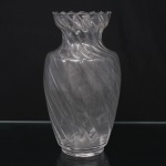 Vaso em vidro incolor moldado, de corpo bojudo com base circular e colo estrangulado, apresentando decoração em espiral torsada em relevo que se desenvolve por toda a superfície. Borda recortada e ondulada, acompanhando o movimento helicoidal da composição. Medidas: Alt.: 26,5 x Diam.: 15 cm.