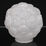 Globo de teto em vidro opalinado moldado, corpo globular com relevo contínuo em composição floral. Superfície inteiramente recoberta por rosas em disposição aglutinada, formando volume escultórico de caráter naturalista. Ornamentação executada em alto-relevo, com pétalas sobrepostas e botões florais distribuídos por toda a circunferência. Bocal circular, apresenta ínfimos bicados causados pelo uso. Interior liso e acabamento monocromático em branco. Medida: Diam.: 16,5 cm.
