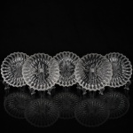 Conjunto de pratos em cristal incolor moldado e prensado, de bordas recortadas, decorados em relevo radial com composição geométrica e floral estilizada ao centro. Composto de cinco(050 unidades. Medida: Diam.: 14 cm.