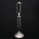 Luminária de mesa em alumínio escovado e metal cromado, composta por base circular abaulada e estrutura vertical formada por hastes tubulares, encimada por corpo cilíndrico protegido por cobertura metálica em forma abaulada. Design modernista e industrial. Apresenta desgastes e sinais de oxidação. Medidas: Alt.: 67 x Diam.: 20 cm.