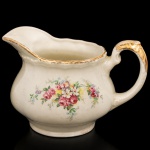 W.H. GRINDLEY, Staffordshire - Inglaterra(Fundada por William Harry Grindley em 1880). Leiteira em faiança inglesa da década de 1940/50, padrão "Creampetal"; esmaltagem de tom marfim, decoração floral policroma com reservas de rosas e flores campestres distribuídas pelo bojo, aplicada por transferência. Borda ondulada, bico vertedor ondulado, com acabamento em douradura, repetido na asa lateral em voluta. Marca da manufatura no verso. Medidas: Alt.: 13 x Comp.: 19,5 x Larg.: 14,5 cm.
