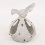 Pot-pourri ou porta-doces em porcelana branca moldada, em formato de trouxa amarrada, com aberturas vazadas em forma de gomos, decoração floral policroma em pequenas reservas e filetes dourados contornando os vazados. Medidas: Alt.: 14,5 x Diam.: 11,5 cm.